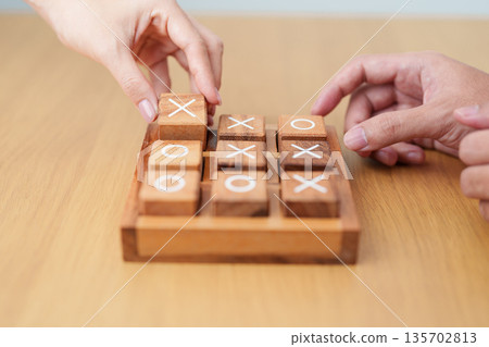 Hand holding and playing wooden block of tic tac toe game. A completed game of noughts and crosses or Xs and Os game. Challenge, Competition, winning, tactic, strategy and recreation concepts 135702813