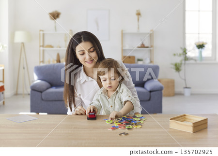 Smiling mother playing with little son at desk, learning alphabet and enjoying fun time at home. Smiling mother playing with little son at desk, learning alphabet and enjoying fun time at home. 135702925