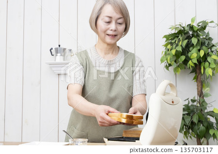 Senior woman making a hot sandwich with a hot sandwich maker Senior woman making a hot sandwich with a hot sandwich maker 135703117
