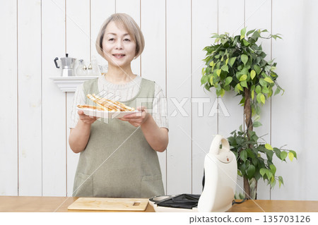一位老婦人正在用熱三明治機製作熱三明治。 一位老婦人正在用熱三明治機製作熱三明治。 135703126