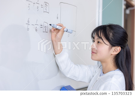 Elementary school student writing fractions on a whiteboard Elementary school student writing fractions on a whiteboard 135703323