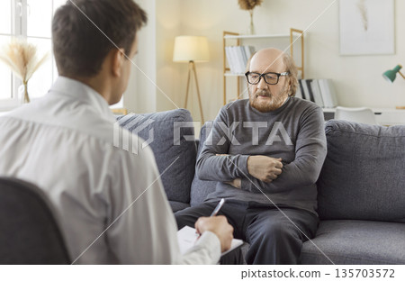 Psychologist making notes consulting senior elderly man patient during therapy session in office Psychologist making notes consulting senior elderly man patient during therapy session in office 135703572