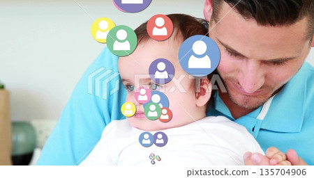 Cradling male holding baby on sofa in bright living room, with colorful floating user profile icons Cradling male holding baby on sofa in bright living room, with colorful floating user profile icons 135704906
