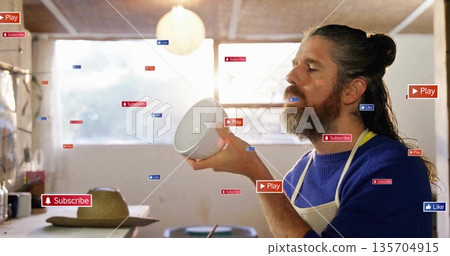 Craftsman in apron holding ceramic bowl in workshop, with Play Subscribe Like overlays, copy space 135704915