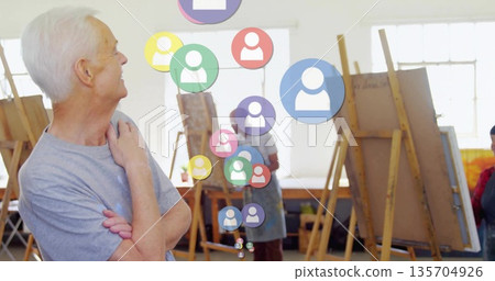 Watching senior male in grey t-shirt crossing arms at art studio, with floating icons, copy space 135704926