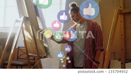 Standing middle-aged artist wearing coat in studio displaying canvas with floating thumbs-up icons Standing middle-aged artist wearing coat in studio displaying canvas with floating thumbs-up icons 135704932