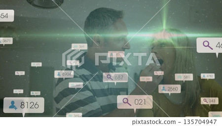 Feeding middle-aged woman pill with man guiding toward mouth in home kitchen, with digital icons 135704947