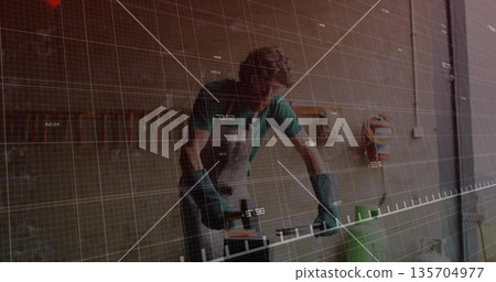 Sanding artisan wearing apron using power sander on wood plank in garage, digital grid overlay 135704977