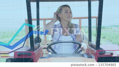 Driving mature woman steering tractor through farmland, with red utility tractor and graph overlay 135704985