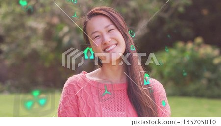 Smiling mid adult Korean woman standing in private garden, with floating green interface icons 135705010