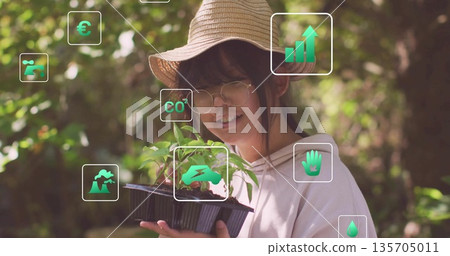 Chinese girl wearing straw hat and round glasses holding seedling tray in garden, with green icons 135705011