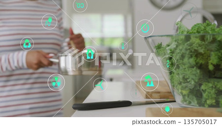 Home cook in striped top stirring soup at kitchen island, with pot, wooden spoon and kale Home cook in striped top stirring soup at kitchen island, with pot, wooden spoon and kale 135705017