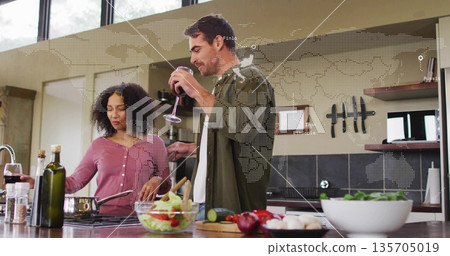 Couple cooking together stirring vegetables and sipping wine at kitchen island, with frying pan 135705019