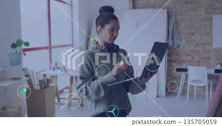 Holding laptop and stylus, creative woman sketching designs in bright loft studio, with headphones 135705059