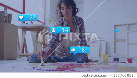 Kneeling artist painting on floor canvas in bright studio, with paint jars and digital icons Kneeling artist painting on floor canvas in bright studio, with paint jars and digital icons 135705091