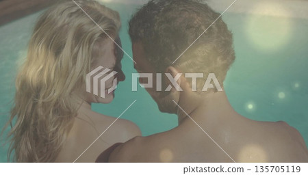 Standing couple facing each other at turquoise pool water with swimwear and lens flare reflections Standing couple facing each other at turquoise pool water with swimwear and lens flare reflections 135705119