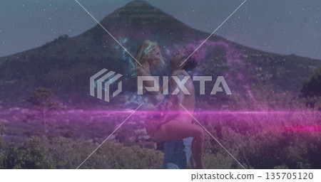 Lifting shirtless man embracing swimsuit woman amid conical mountain shrubs, with pink purple glow Lifting shirtless man embracing swimsuit woman amid conical mountain shrubs, with pink purple glow 135705120