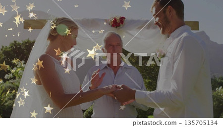 Exchanging wedding rings bride and groom standing outdoors under wooden arch, with floral decor Exchanging wedding rings bride and groom standing outdoors under wooden arch, with floral decor 135705134