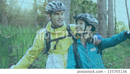 Smiling couple standing on forest path with helmets, backpacks, displaying AR data overlays Smiling couple standing on forest path with helmets, backpacks, displaying AR data overlays 135705136