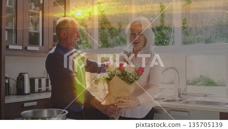 Surprising senior man gifting bouquet of pink and white roses to mature woman in home kitchen Surprising senior man gifting bouquet of pink and white roses to mature woman in home kitchen 135705139