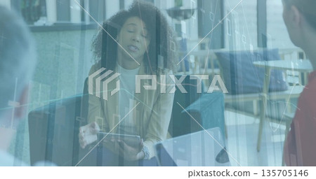 Presenting woman wearing khaki blazer sharing data charts in office lounge, with tablet and laptop 135705146