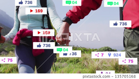 Walking mature hiking couple holding hands on grassy trail with packs poles smartwatch social icons 135705168