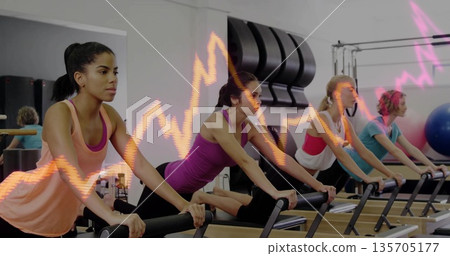 Stretching four women performing leg stretches on Pilates reformer machines in studio, with mirror Stretching four women performing leg stretches on Pilates reformer machines in studio, with mirror 135705177