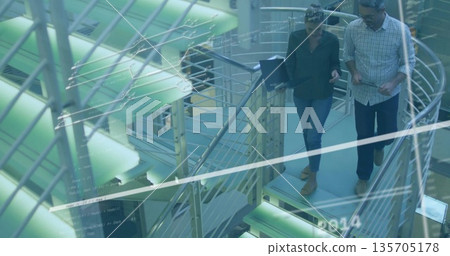 Descending staircase professionals consulting laptop and tablet in office atrium, copy space Descending staircase professionals consulting laptop and tablet in office atrium, copy space 135705178