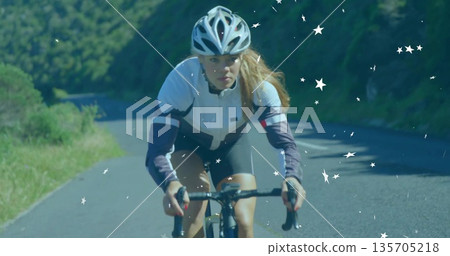 Pedaling female athlete wearing helmet leaning over drop bars on hillside road, with star overlays Pedaling female athlete wearing helmet leaning over drop bars on hillside road, with star overlays 135705218