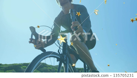 Pedaling road bicyclist gripping drop handlebars on road beside hills under blue sky, golden stars 135705231