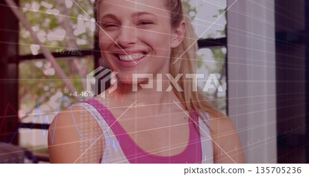 Smiling athletic woman wearing pink tank top analyzing graph overlay in room, with window foliage 135705236