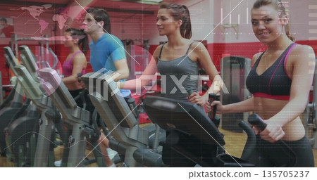 Four exercisers wearing workout clothes working out on ellipticals in gym, with digital consoles 135705237