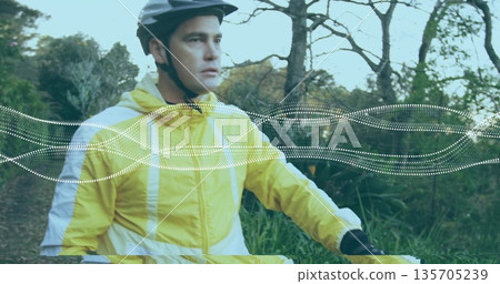 Riding light-skinned cyclist pedaling forest trail, with helmet, windbreaker, handlebars and gloves 135705239