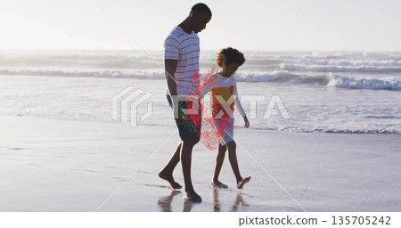 Walking mid adult man and boy strolling along sandy shoreline, with wet sand reflecting ocean waves 135705242