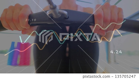 Holding cardio handlebars, woman in black activewear exercising in gym, with digital metric overlay 135705247
