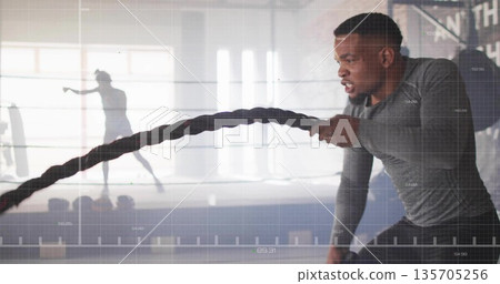 Swinging battle rope man building strength in gym by windows with grid overlay, copy space 135705256