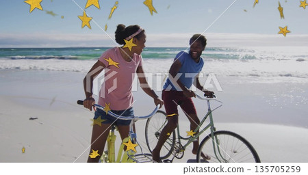 Smiling couple wearing summer clothes riding cruiser bicycles at beach, with golden star graphics Smiling couple wearing summer clothes riding cruiser bicycles at beach, with golden star graphics 135705259
