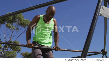Lifting man wearing sleeveless green shirt pulling upward on metal fitness bars at park Lifting man wearing sleeveless green shirt pulling upward on metal fitness bars at park 135705265