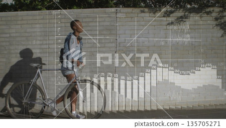 Walking casual woman pushing bicycle by brick wall, overlaid bar chart and line graph, copy space 135705271