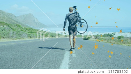 Walking male cyclist carrying bicycle over shoulder along coastal highway, wearing cycling outfit 135705302