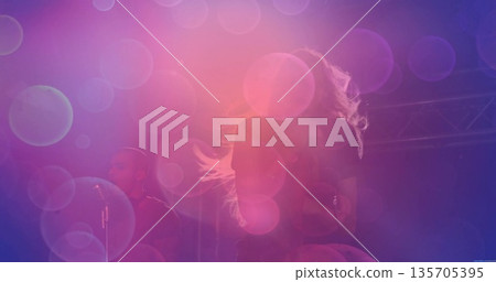 Performing female musician singing into microphone on stage, with purple-pink lighting and trusses Performing female musician singing into microphone on stage, with purple-pink lighting and trusses 135705395