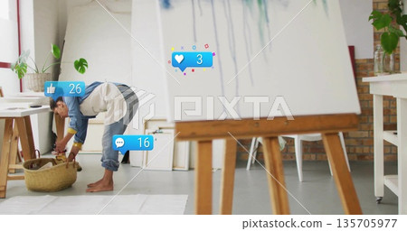 Bending artist sorting brushes in wicker basket in art studio, with easel paint dripped canvas Bending artist sorting brushes in wicker basket in art studio, with easel paint dripped canvas 135705977