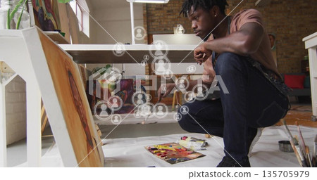 Crouching artist painting canvas on studio floor, with brush, art supplies and user icons overlay Crouching artist painting canvas on studio floor, with brush, art supplies and user icons overlay 135705979