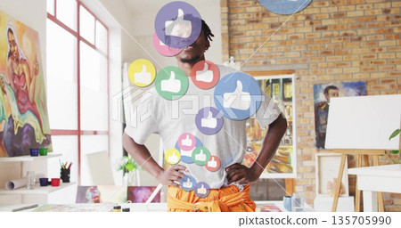 Standing mid adult Black male artist surveying art studio, with floating thumbs-up icons 135705990