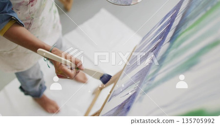 Applying strokes artist painting on canvas in studio, with paintbrush, apron, dropcloth, copy space 135705992