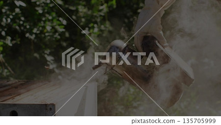 Holding gloved hand gripping metal smoker emitting smoke over wooden hive box in garden, copy space 135705999