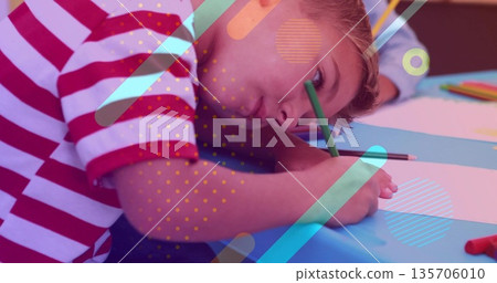 Drawing boy in striped T-shirt resting on arm at classroom table, with green pencil, paper sheets Drawing boy in striped T-shirt resting on arm at classroom table, with green pencil, paper sheets 135706010