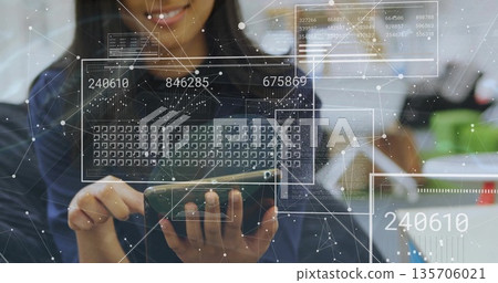 Holding smartphone tapping keyboard grid at office desk in dark blouse, with holographic panels Holding smartphone tapping keyboard grid at office desk in dark blouse, with holographic panels 135706021