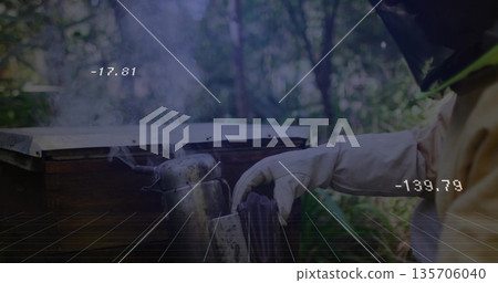 Beekeeper in suit manipulating hive tool beside wooden hive box at apiary, metal smoker, copy space Beekeeper in suit manipulating hive tool beside wooden hive box at apiary, metal smoker, copy space 135706040