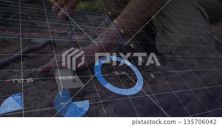 Gripping gardener's hands pressing metal dibber into loose soil at garden bed, with data overlays 135706042